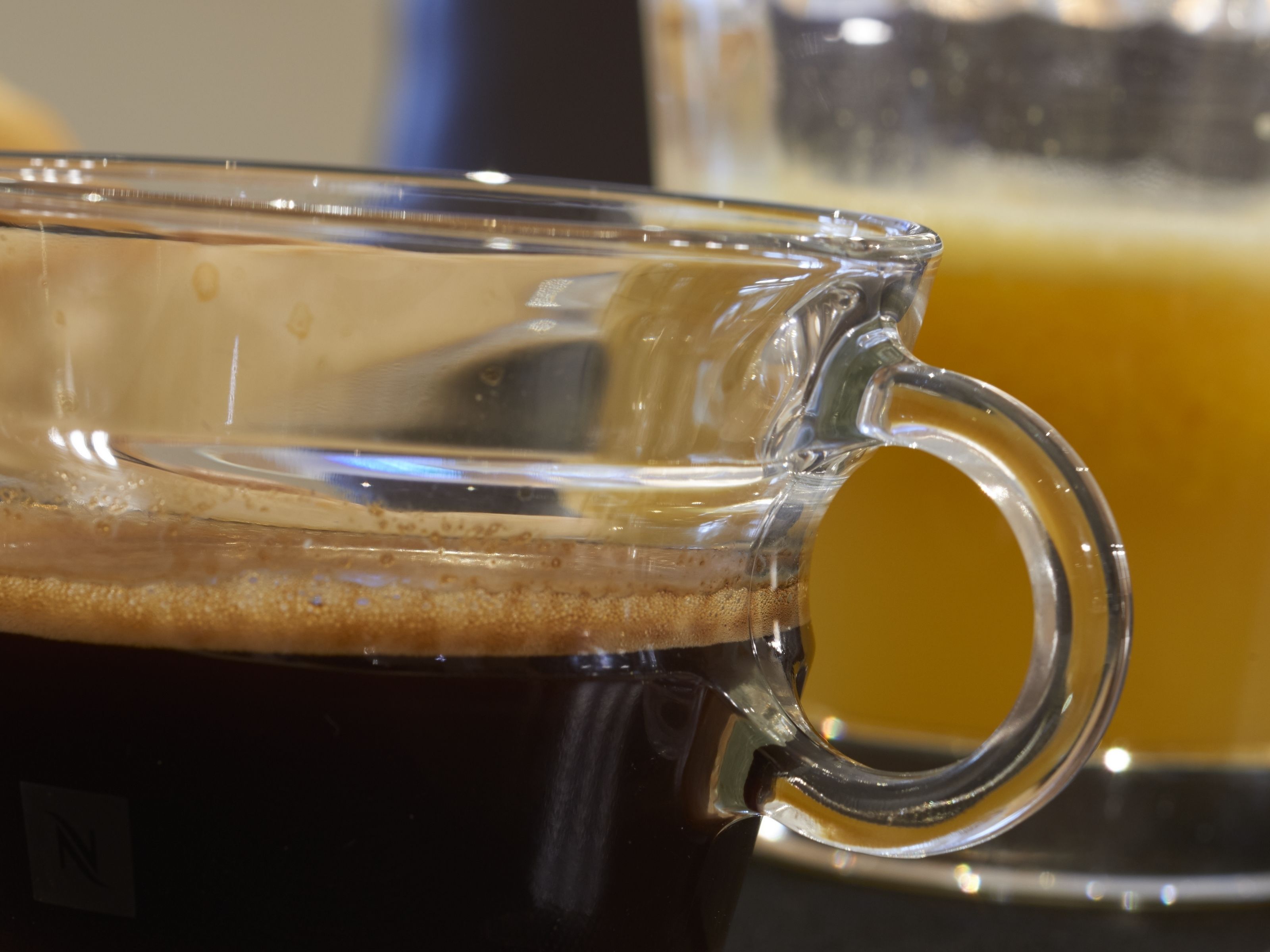 Une tasse en verre remplie d’un liquide sombre, peut-être du café, avec une mousse à la surface.