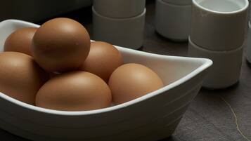 A white ceramic bowl containing several brown eggs on a dark countertop.