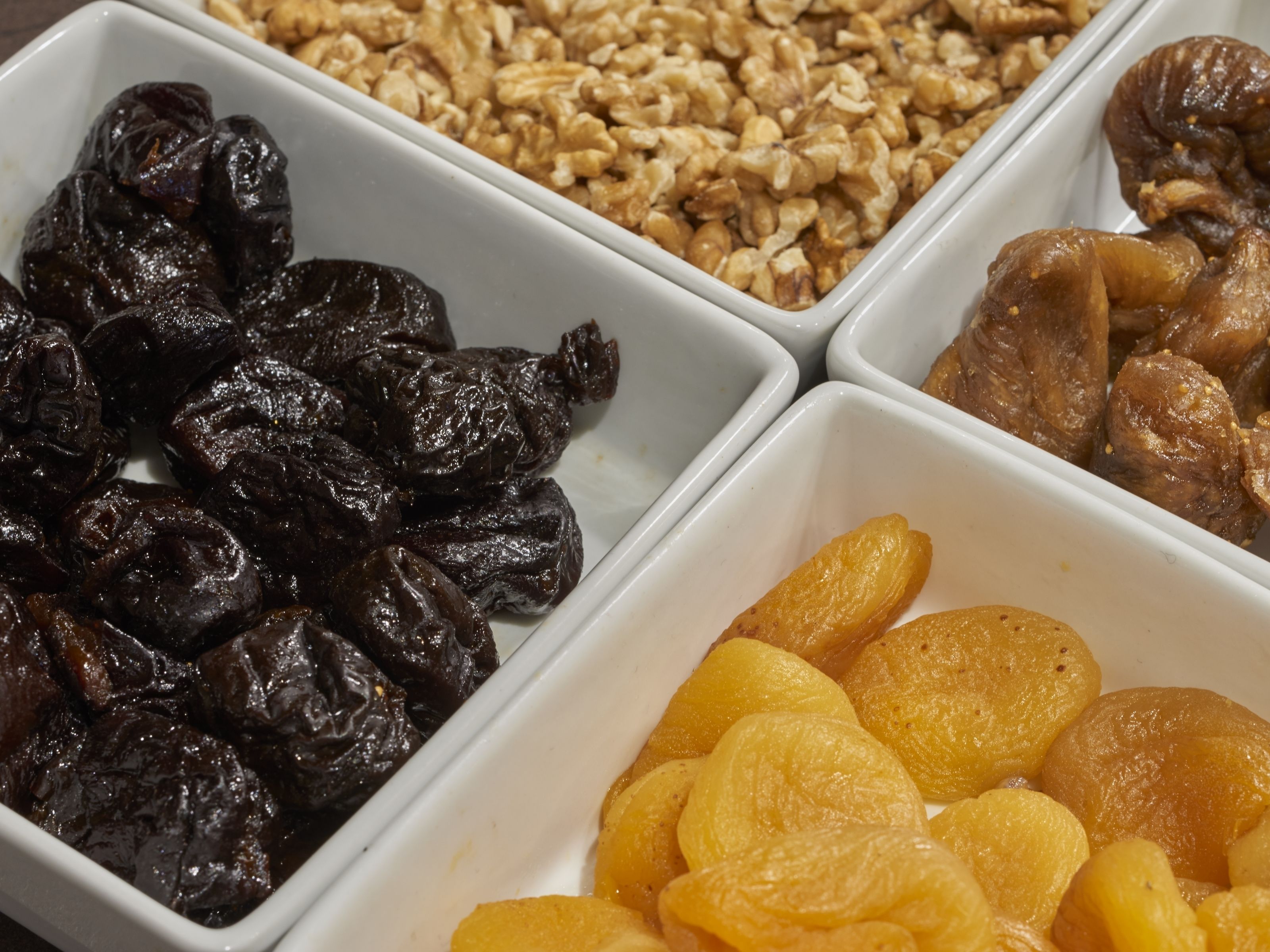 Três recipientes retangulares brancos com frutas secas.