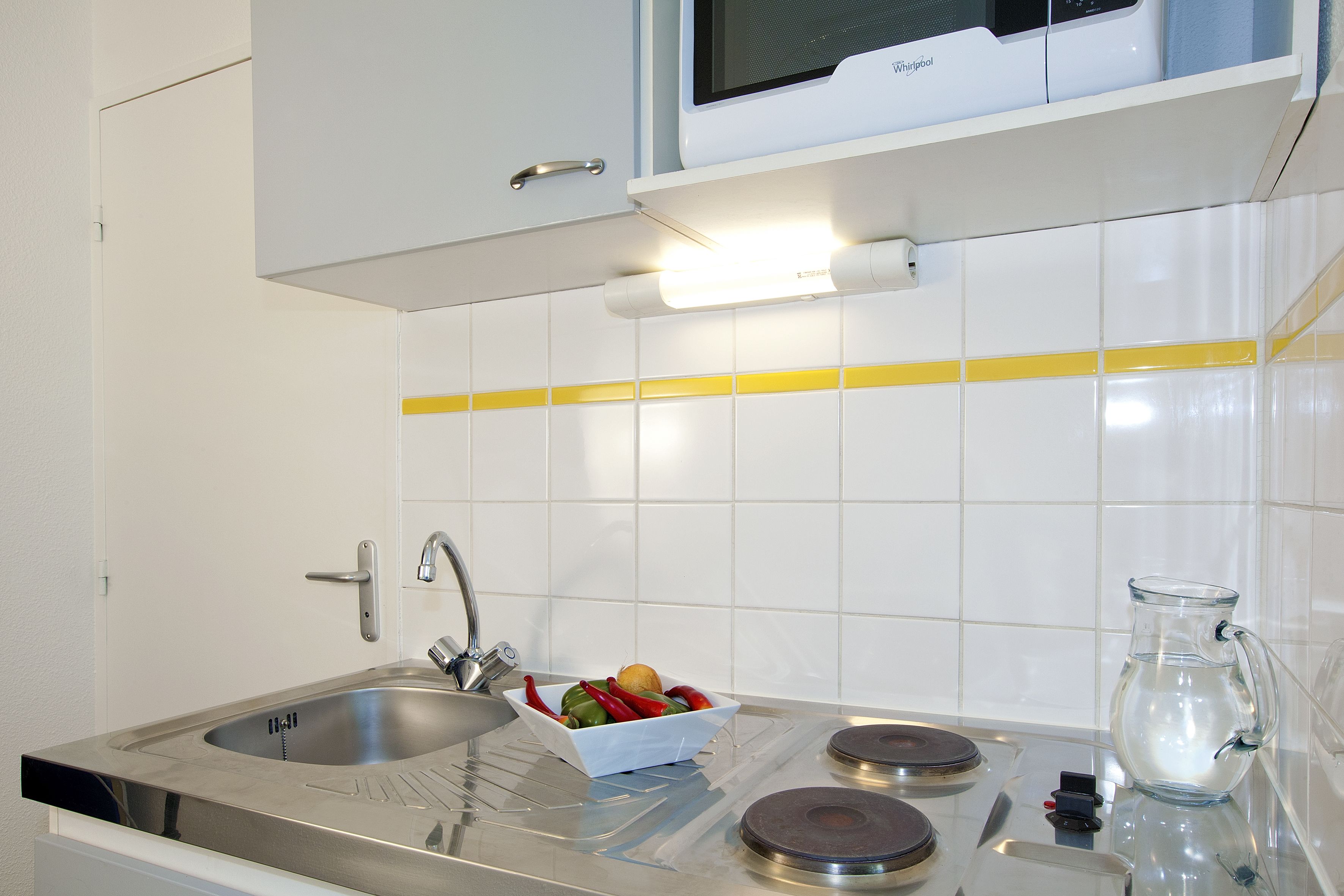 A modern kitchen with a stainless steel sink, a microwave, and a glass pitcher on the counter.
