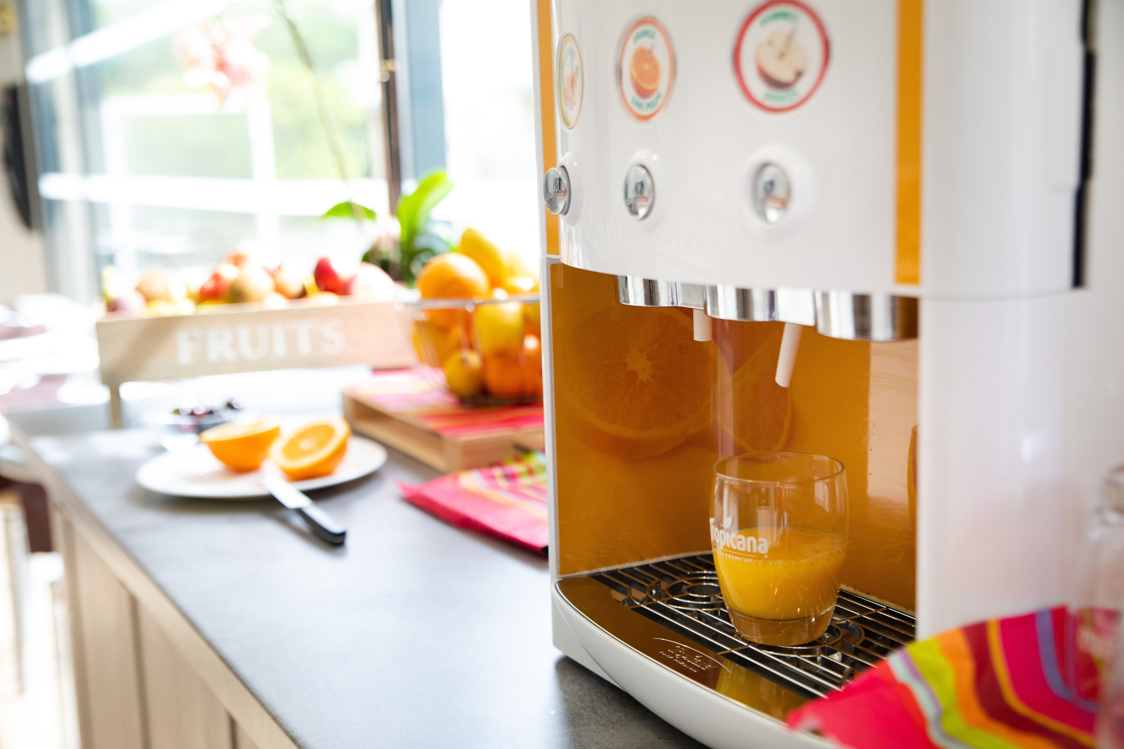 A kitchen with a fruit juicer dispensing orange juice into a glass.