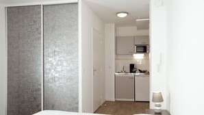 Un dormitorio con cama, armario y una kitchenette al fondo.