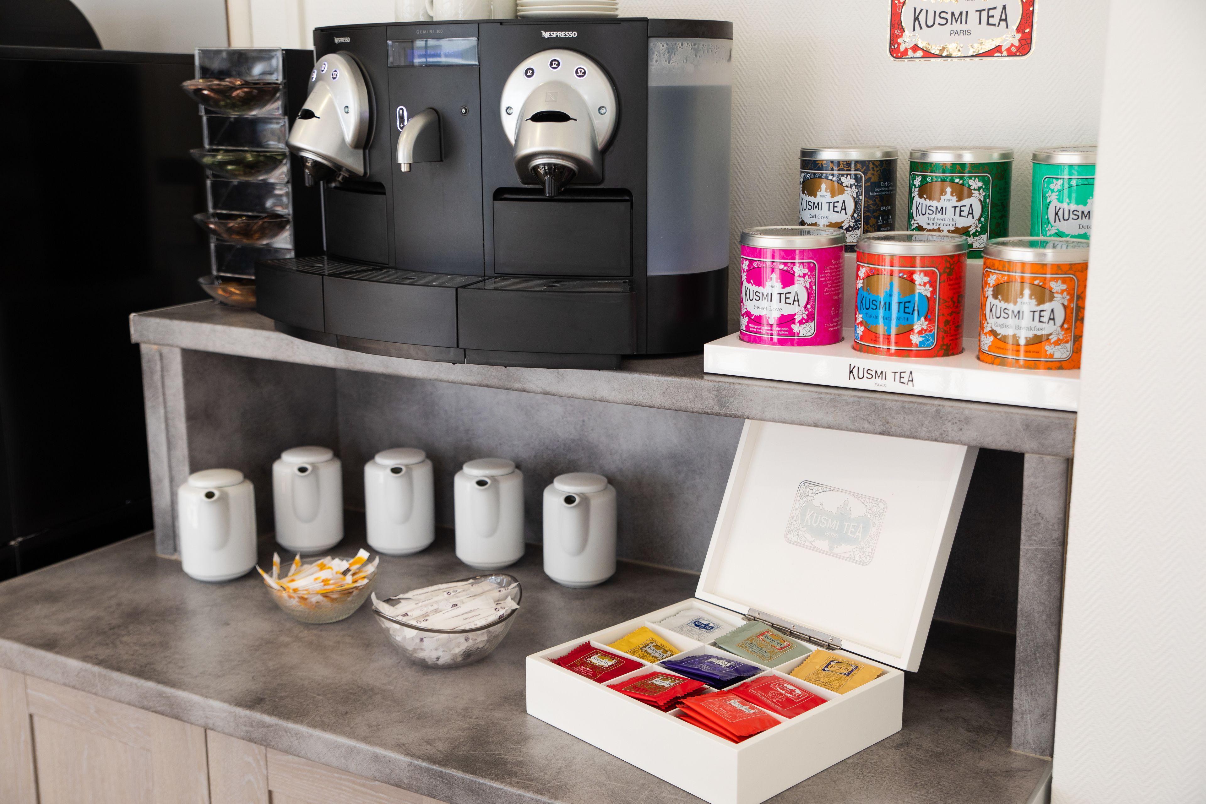 Une machine à café, des distributeurs de thé et une variété de boîtes à thé sont disposés sur un comptoir.