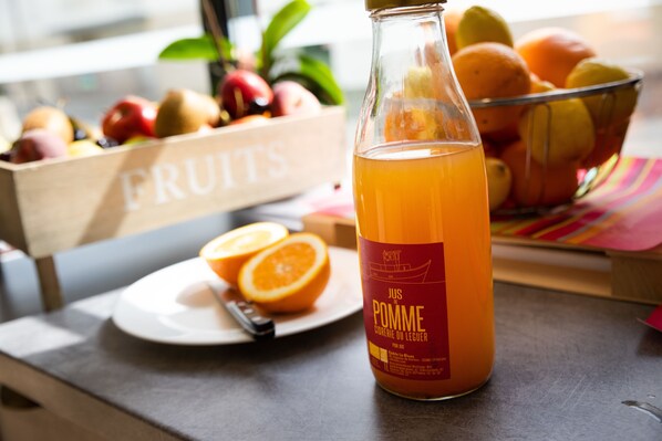A bottle of juice with a label, a plate with a half orange, and a fruit basket in the background.