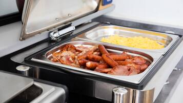 Un bufé con bandejas de comida, incluyendo salchichas y huevos revueltos.