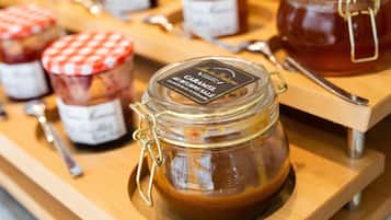 A display of caramel sauce jars with metal lids and handles, arranged on a wooden board with spoons beside them.