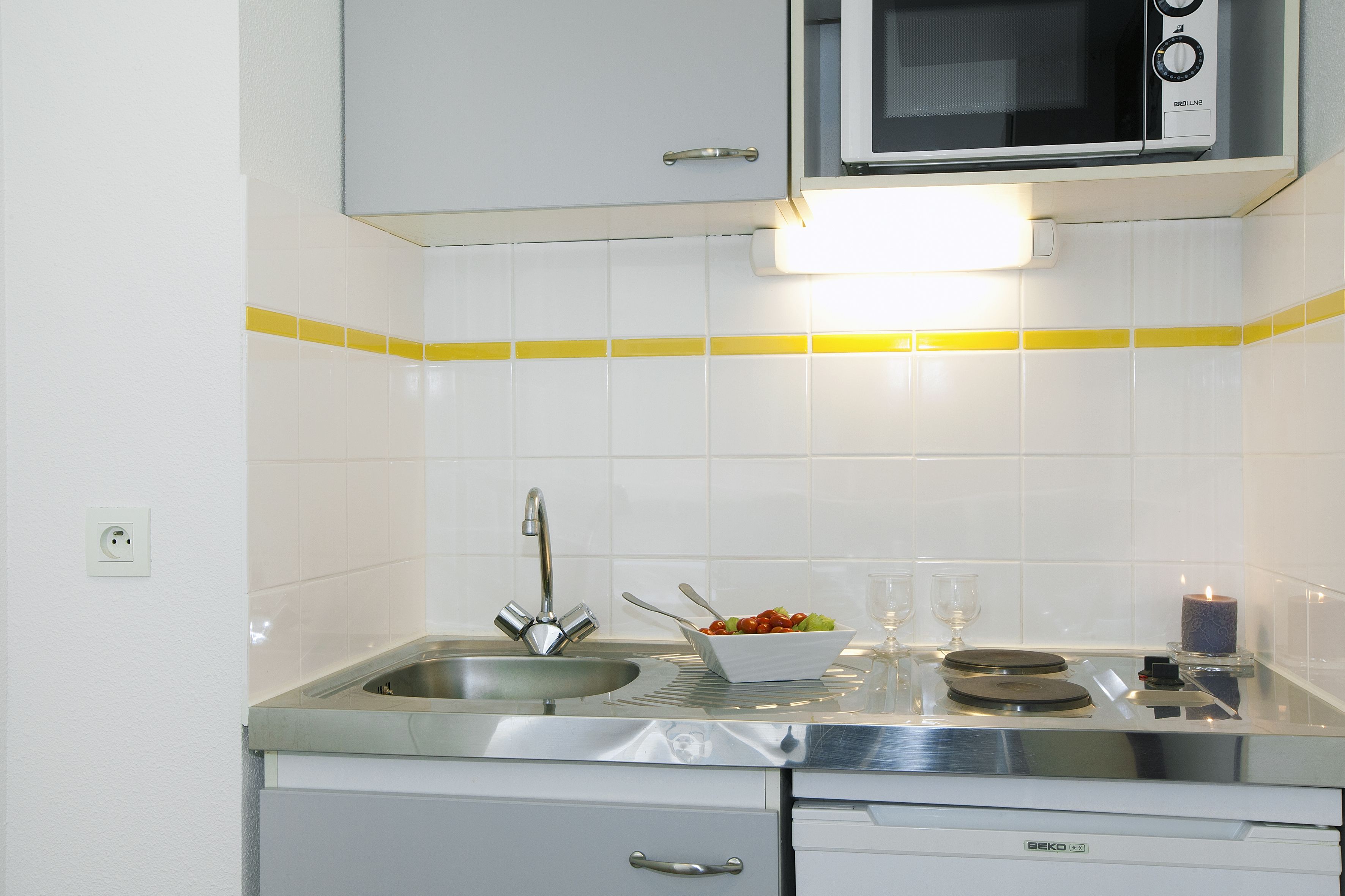 Una cucina compatta con microonde, lavello e una ciotola di frutta sul piano di lavoro.