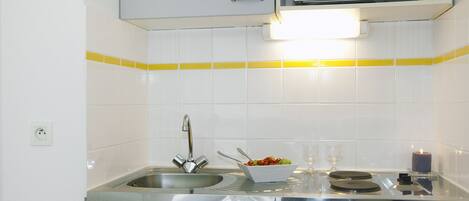 A compact kitchen with a microwave, sink, and a bowl of fruit on the counter.