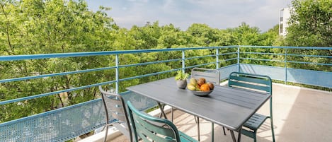 An outdoor balcony with a table and chairs, a bowl of fruit, and a potted plant.