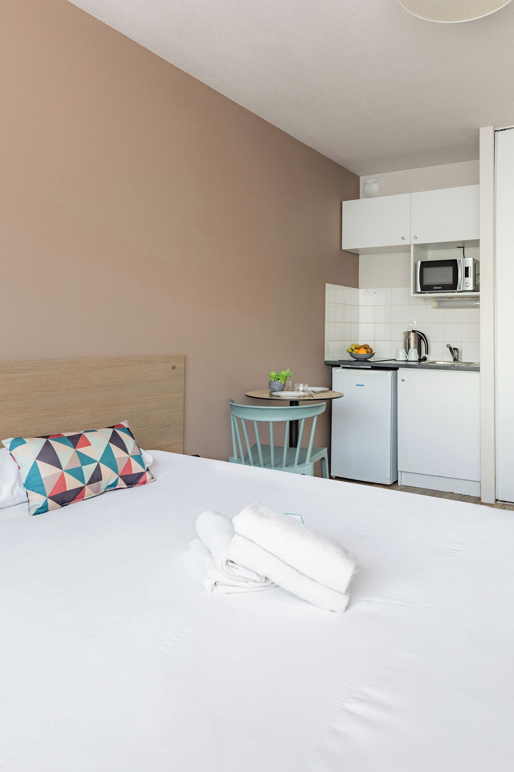 Una habitación de hotel con cama, una mesita con silla, microondas y refrigerador.