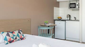 Una habitación de hotel con cama, una mesita con silla, microondas y refrigerador.