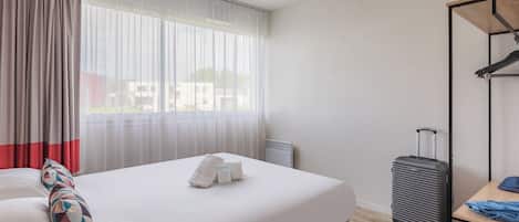 Una camera d'albergo con un letto, una valigia, un tavolo e una finestra con tende.
