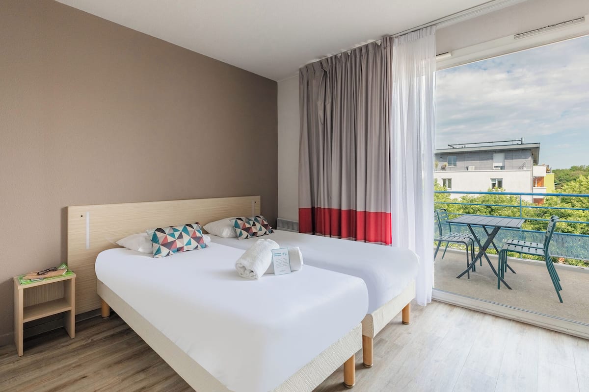 A modern hotel room with a large bed, a small side table, and a balcony with a table and chairs.