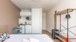 A compact hotel room with a bed, a small kitchenette, a wooden shelf, and a wardrobe. - Appart'City Classic La Rochelle Centre (La Rochelle)