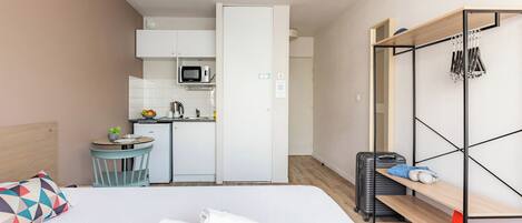 Une chambre d’hôtel compacte comprenant un lit, une petite kitchenette, une étagère en bois et une armoire.