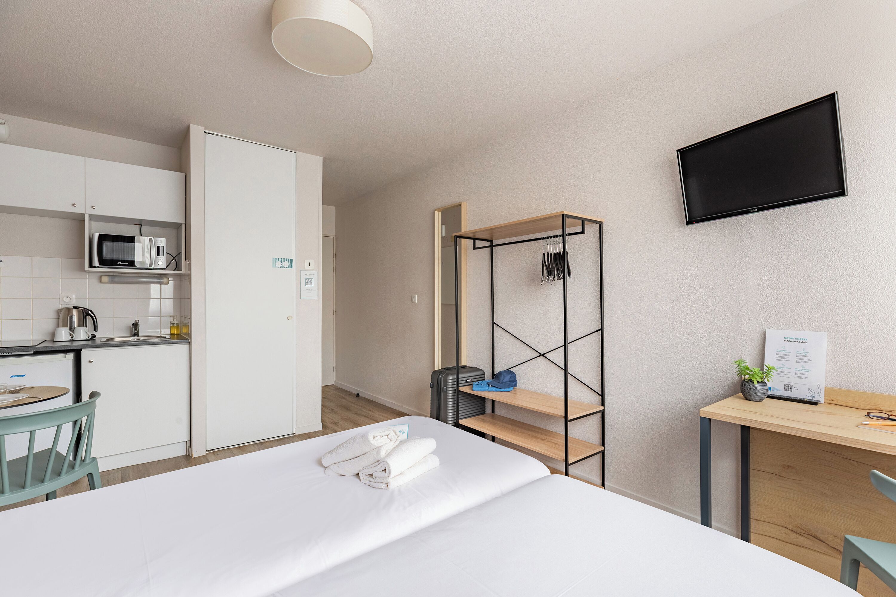 Habitació d'hotel amb un llit, escriptori amb ordinador, televisió, petita cuina i armari.