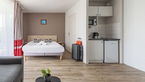 A hotel room with a bed, a small kitchenette, a suitcase, and a plant on a side table. - Appart'City Classic La Rochelle Centre (La Rochelle)