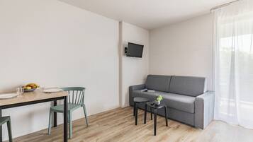 A modern living room with a grey sofa, a wooden dining table with chairs, a small side table, and a mounted TV.