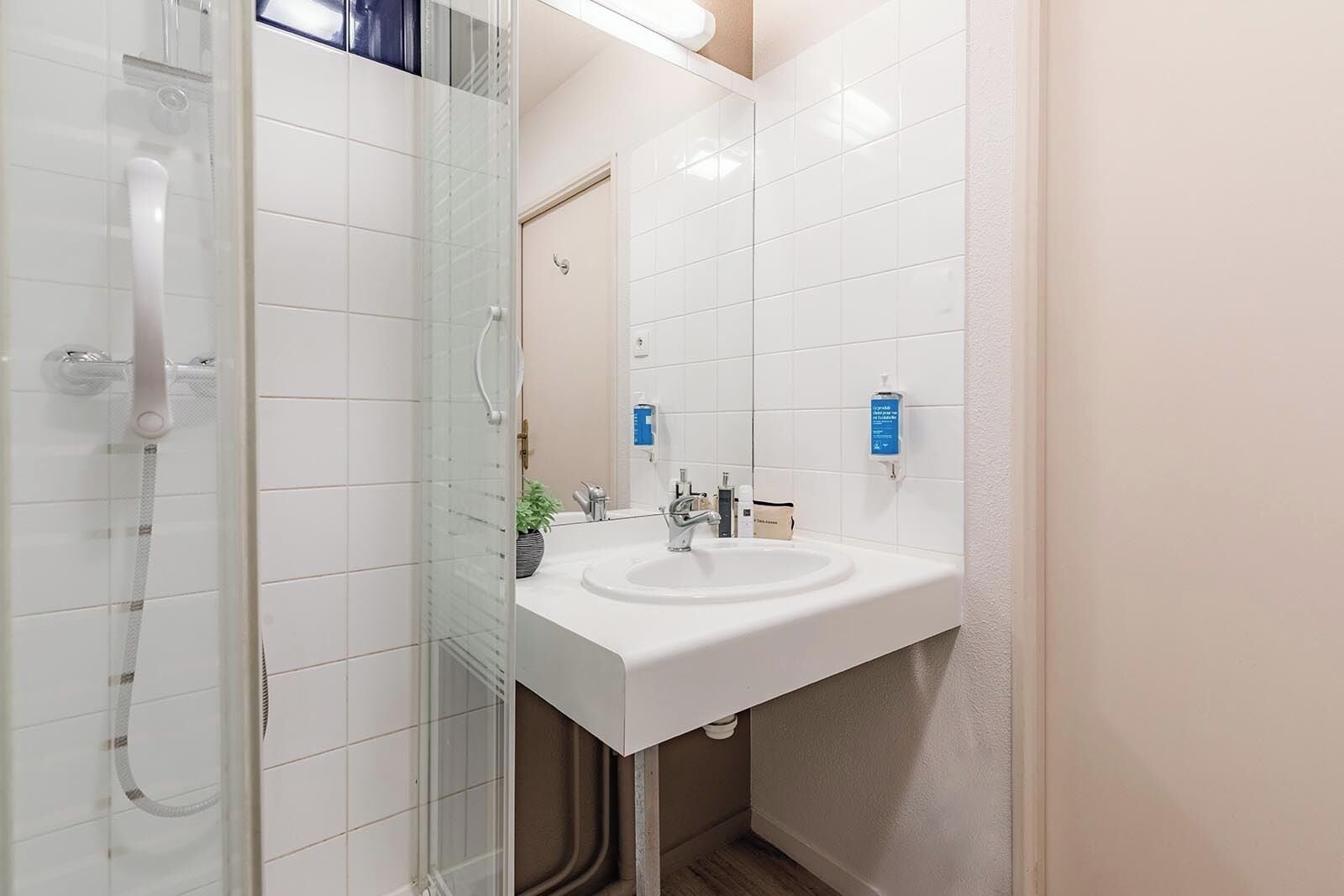 Een moderne badkamer met een douchecabine van glas, een witte wastafel en een spiegel.