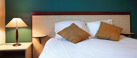 A neatly made bed with two pillows, a bedside lamp, and a wooden nightstand.