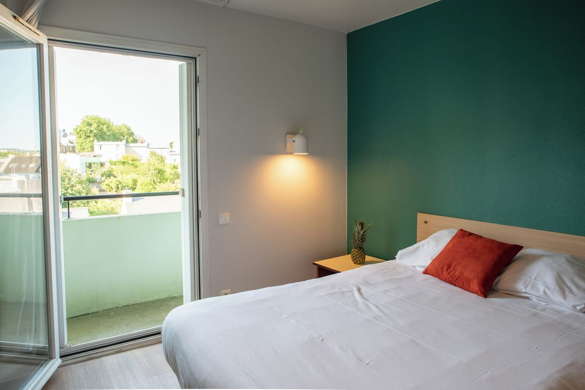 Een hotelkamer met een bed, nachtkastje, lamp en uitzicht.