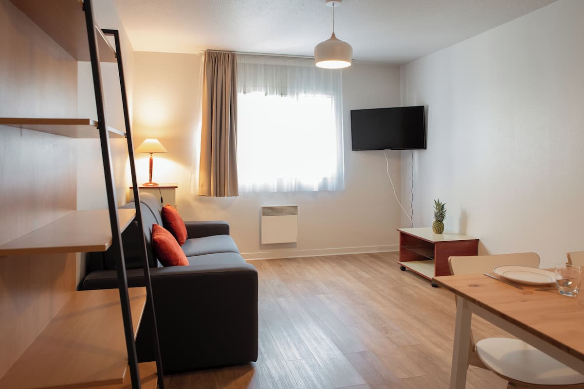 Een moderne woonkamer met een bank, een eettafel en een aan de muur bevestigde televisie.