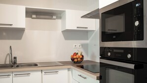 Una cocina moderna con armarios blancos, un lavamanos de acero inoxidable, un microondas negro y un horno.