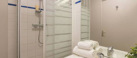 Un baño moderno con cabina de ducha de vidrio, un lavamanos blanco con grifo plateado y un espejo que refleja la habitación.