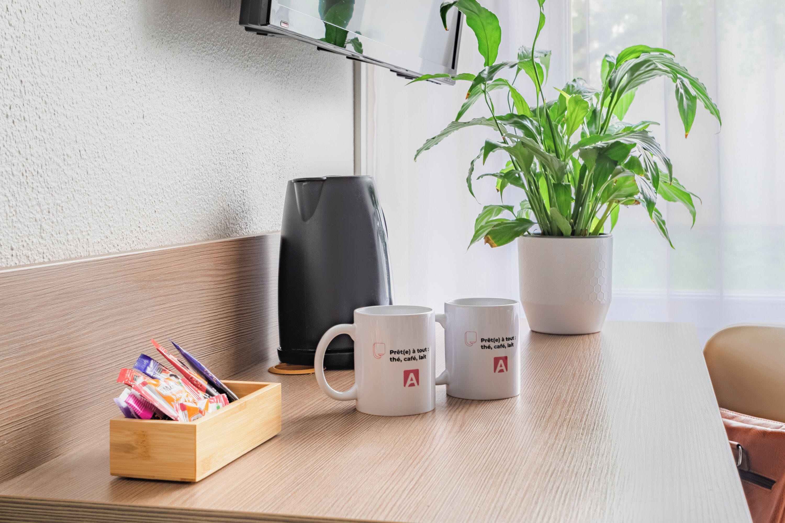 Un bureau en bois, avec deux tasses blanches, un porte-stylos en bois, une machine à café noire et une plante en pot.