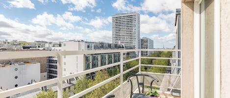 Un balcon offrant une vue sur le paysage urbain, avec notamment un grand immeuble visible au loin.