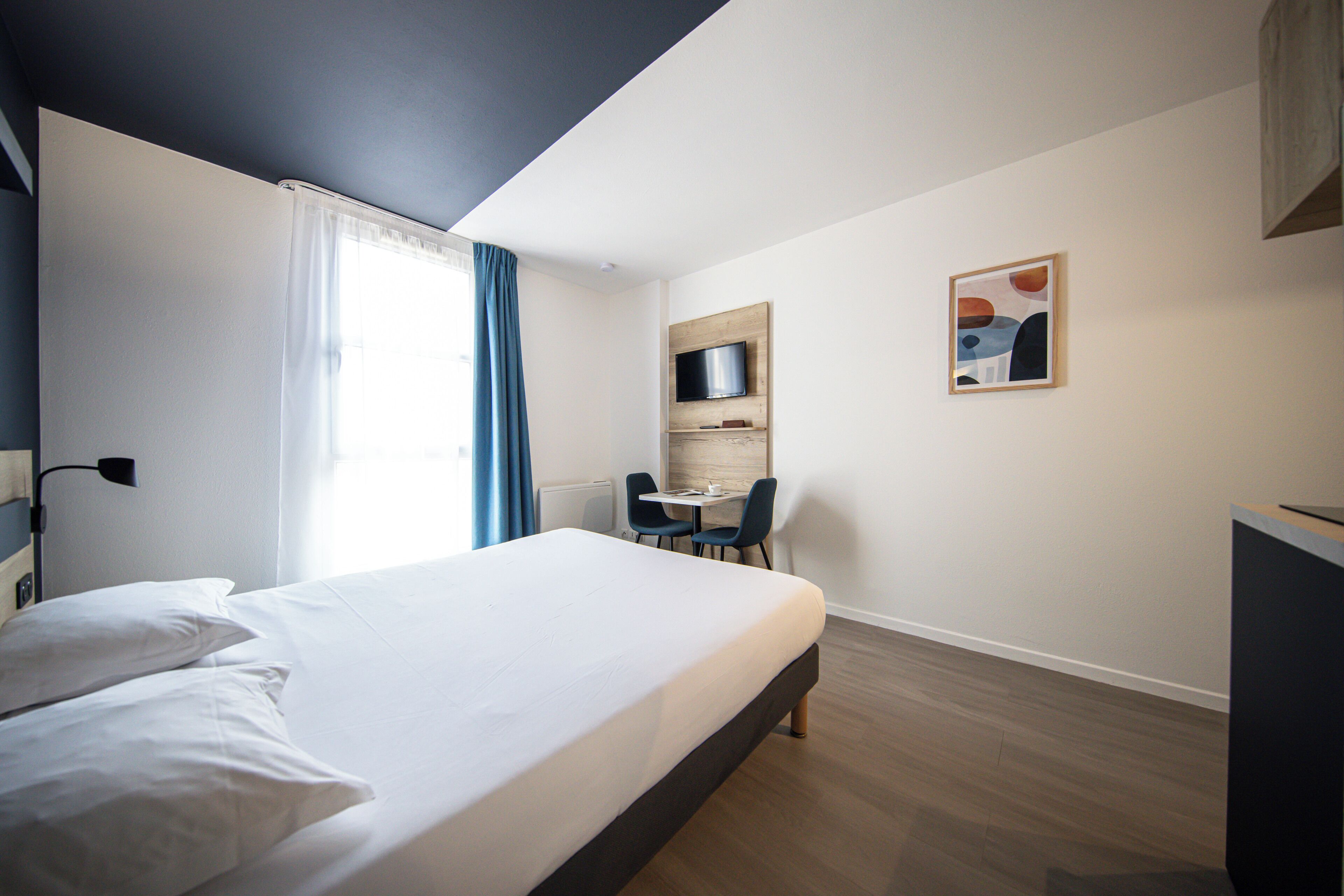 Een hotelkamer met een bed, bureau, stoel, televisie en een schilderij aan de muur.