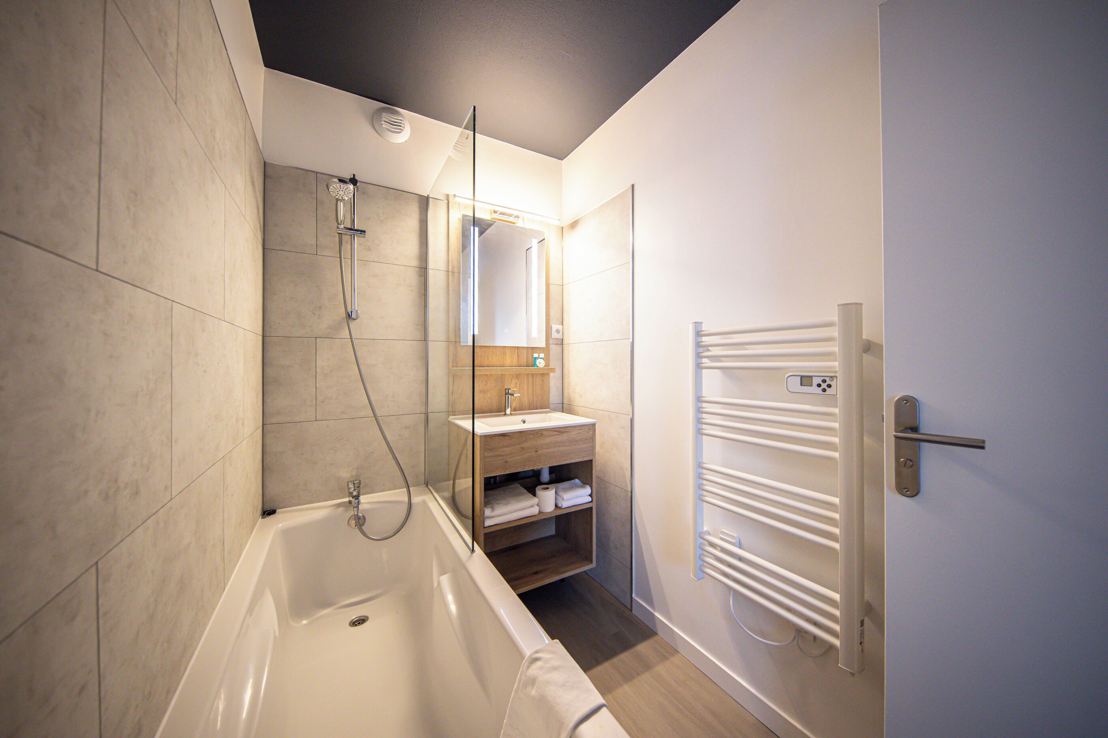 A modern bathroom with a bathtub, a glass-enclosed shower, a wooden vanity, and a towel rack.