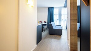 A modern hotel room with a sofa, a dining area, and a view of the outdoors. - City Residence Nancy (Nancy)