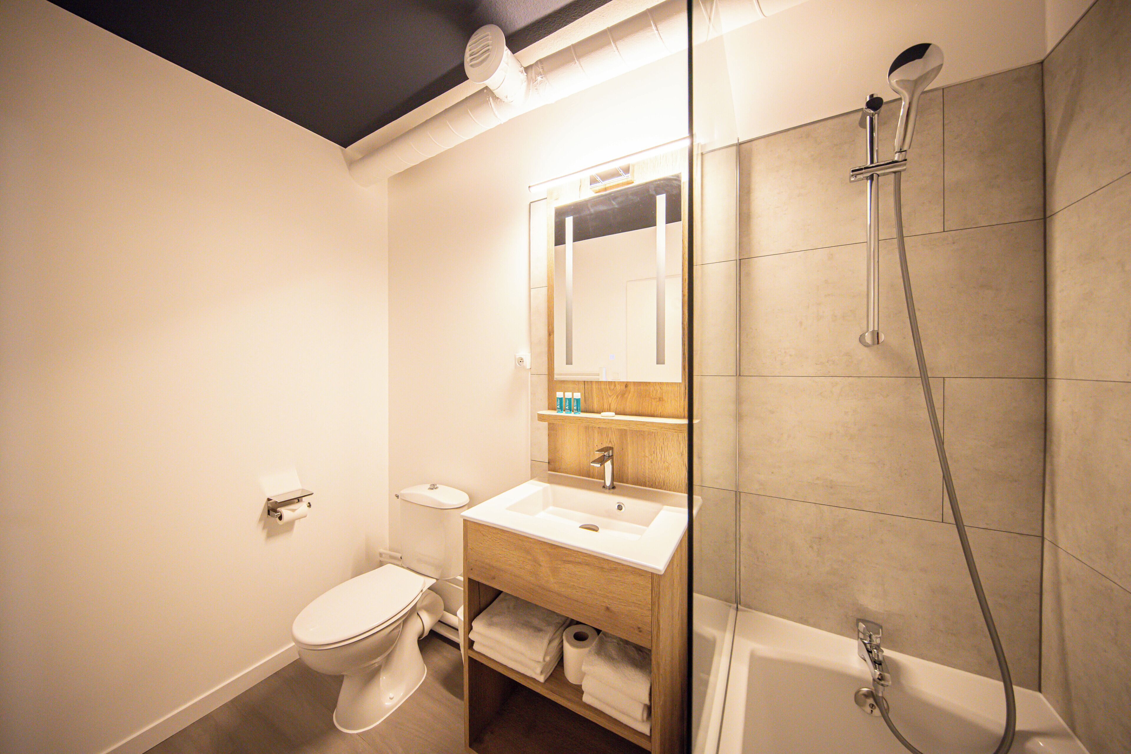 A bathroom with a toilet, sink, mirror, and shower.