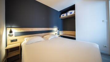 Quarto com cama, mesas de cabeceira, prateleira na parede e tomadas.