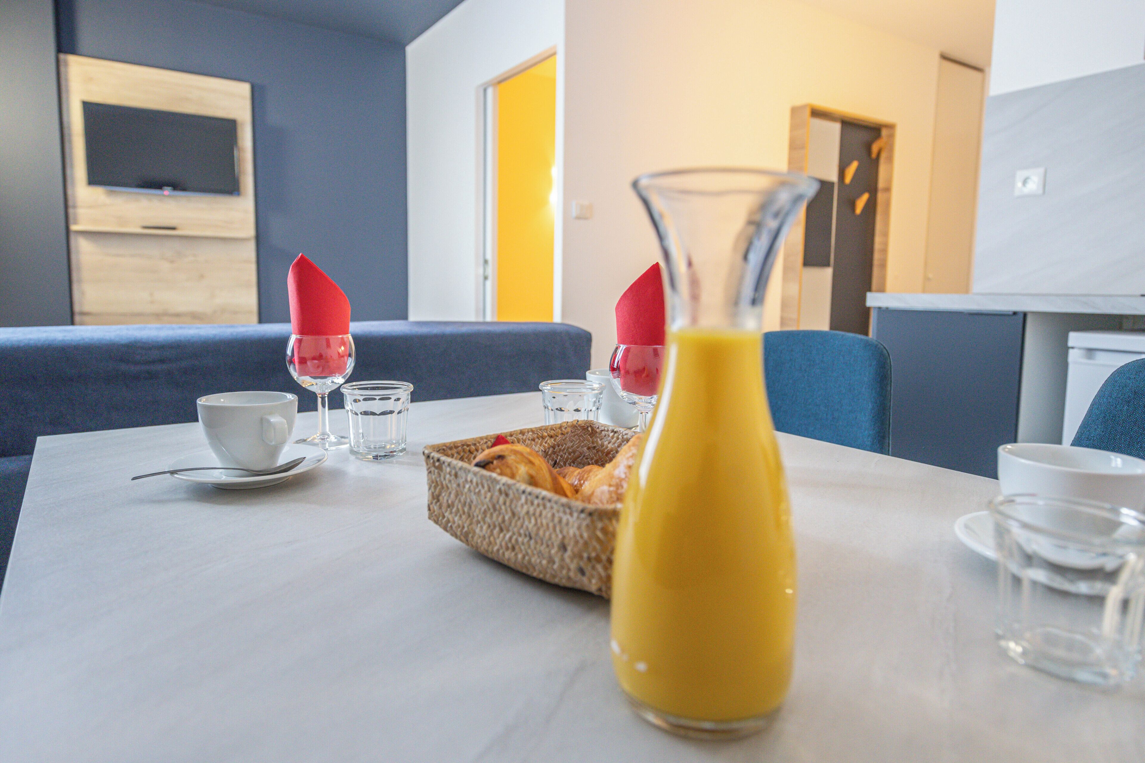 A dining table with breakfast items, a bottle of juice, and a TV in the background.