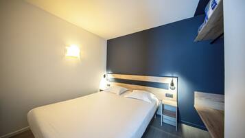 A hotel room with a bed, bedside tables, a nightstand, and a wall-mounted shelf.