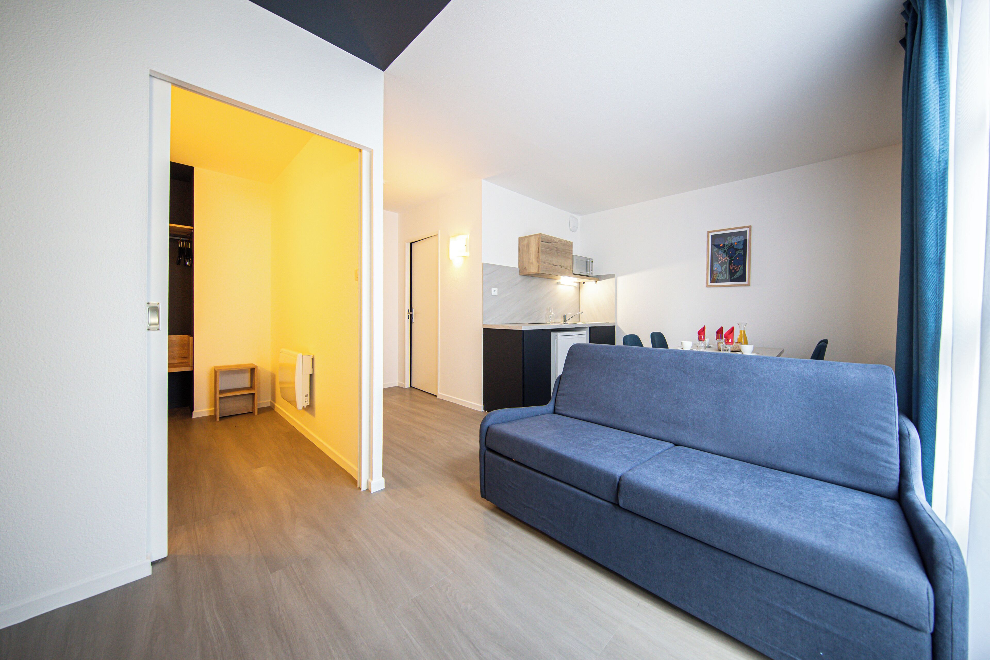 A modern living room with a sofa, a kitchen area, and a dining table with chairs.