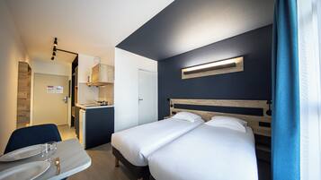 A hotel room with a bed, bedside table, and a small kitchenette.