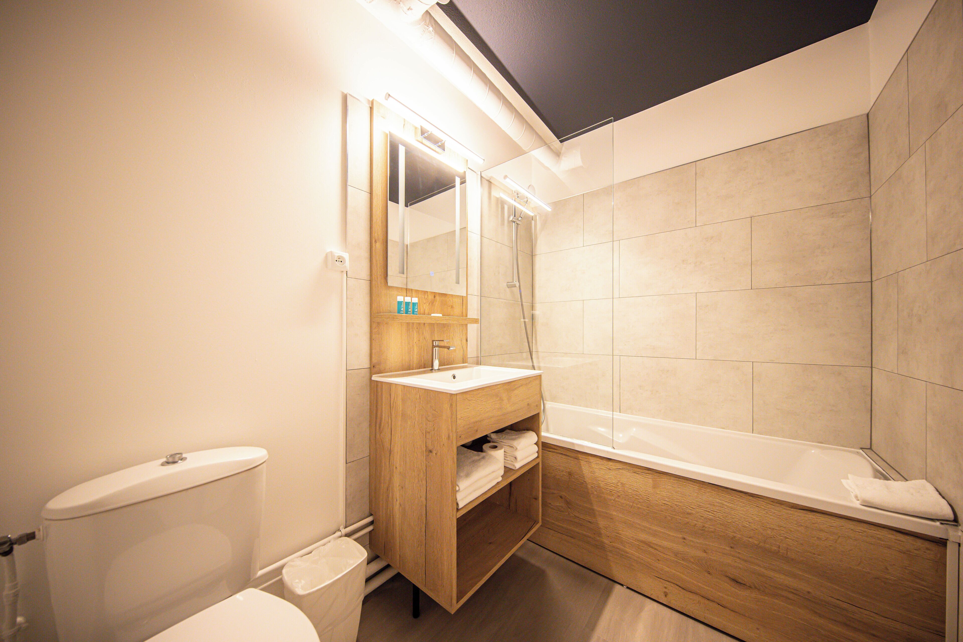 A modern bathroom with a toilet, sink, mirror, and bathtub.