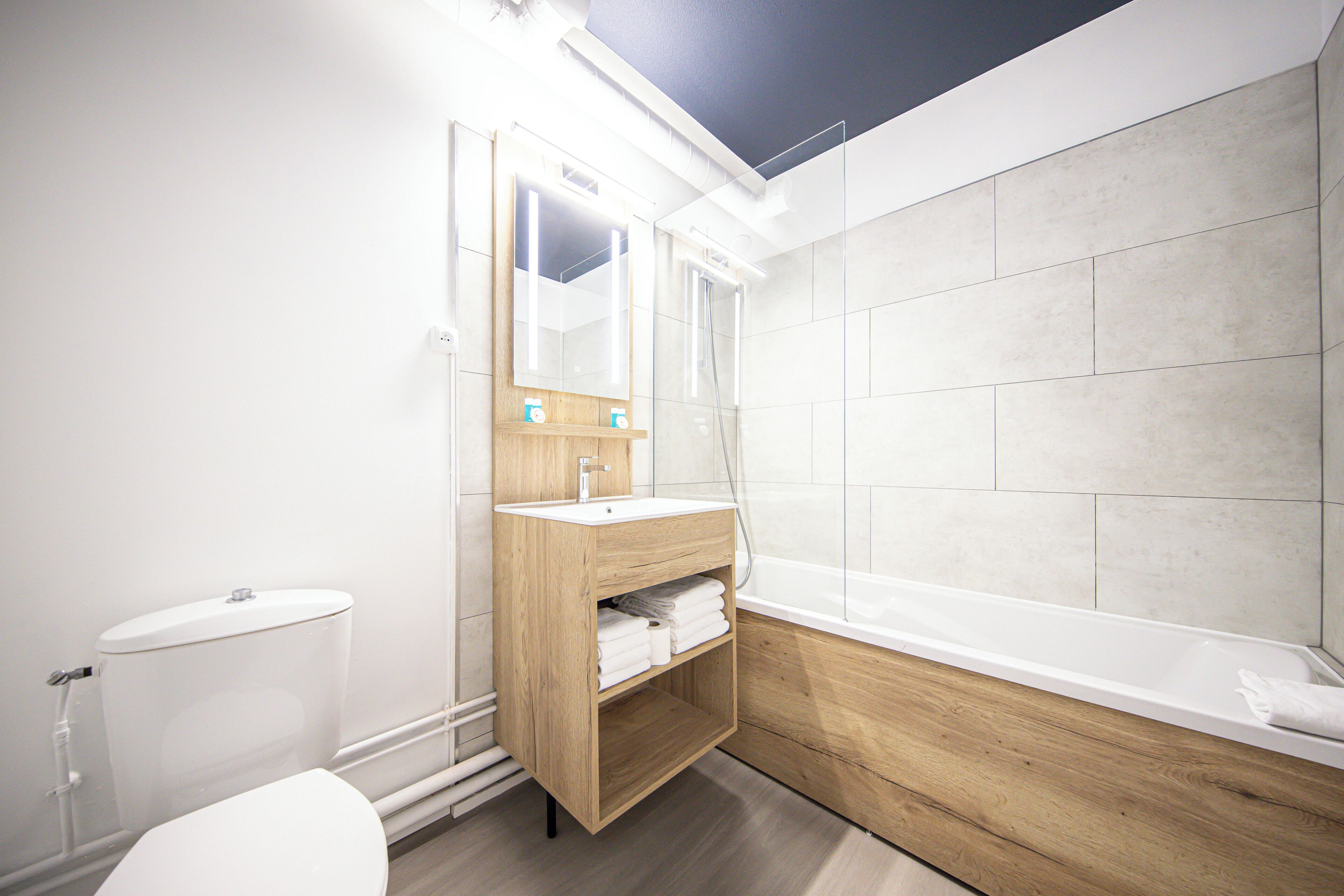 Une salle de bain moderne avec un meuble-lavabo en bois, des toilettes blanches et une baignoire.