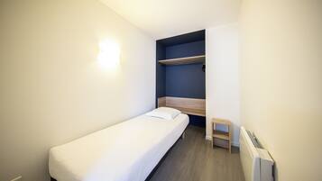 Een kleine kamer met een enkel bed, een houten hoofdbord, een nachtkastje en een inbouwkast.