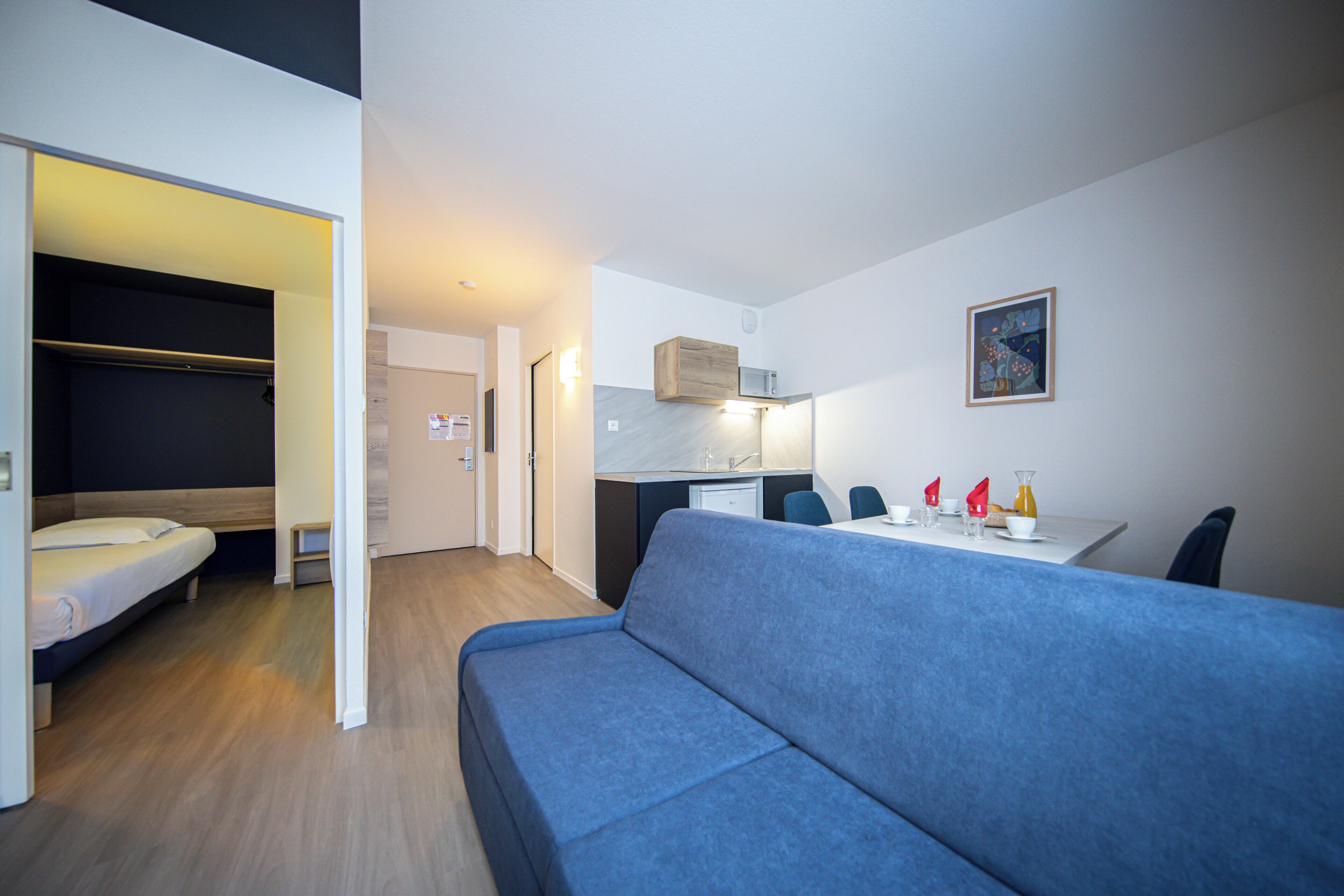 A compact room with a bed, a blue sofa, a small kitchenette, and a dining area.