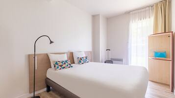 Una habitación de hotel con una cama grande, una mesita de noche, una lámpara, una maleta y un armario.