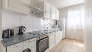 A modern kitchen with white cabinets, a built-in oven, a washing machine, and a coffee maker. - Appart'City Classic Rennes Ouest (Rennes)