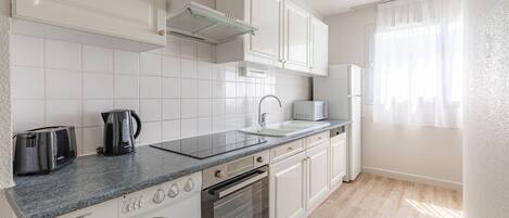 A modern kitchen with white cabinets, a built-in oven, a washing machine, and a coffee maker.