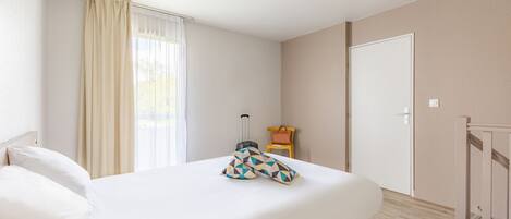 A hotel room with a bed, a suitcase, a chair, and a door.