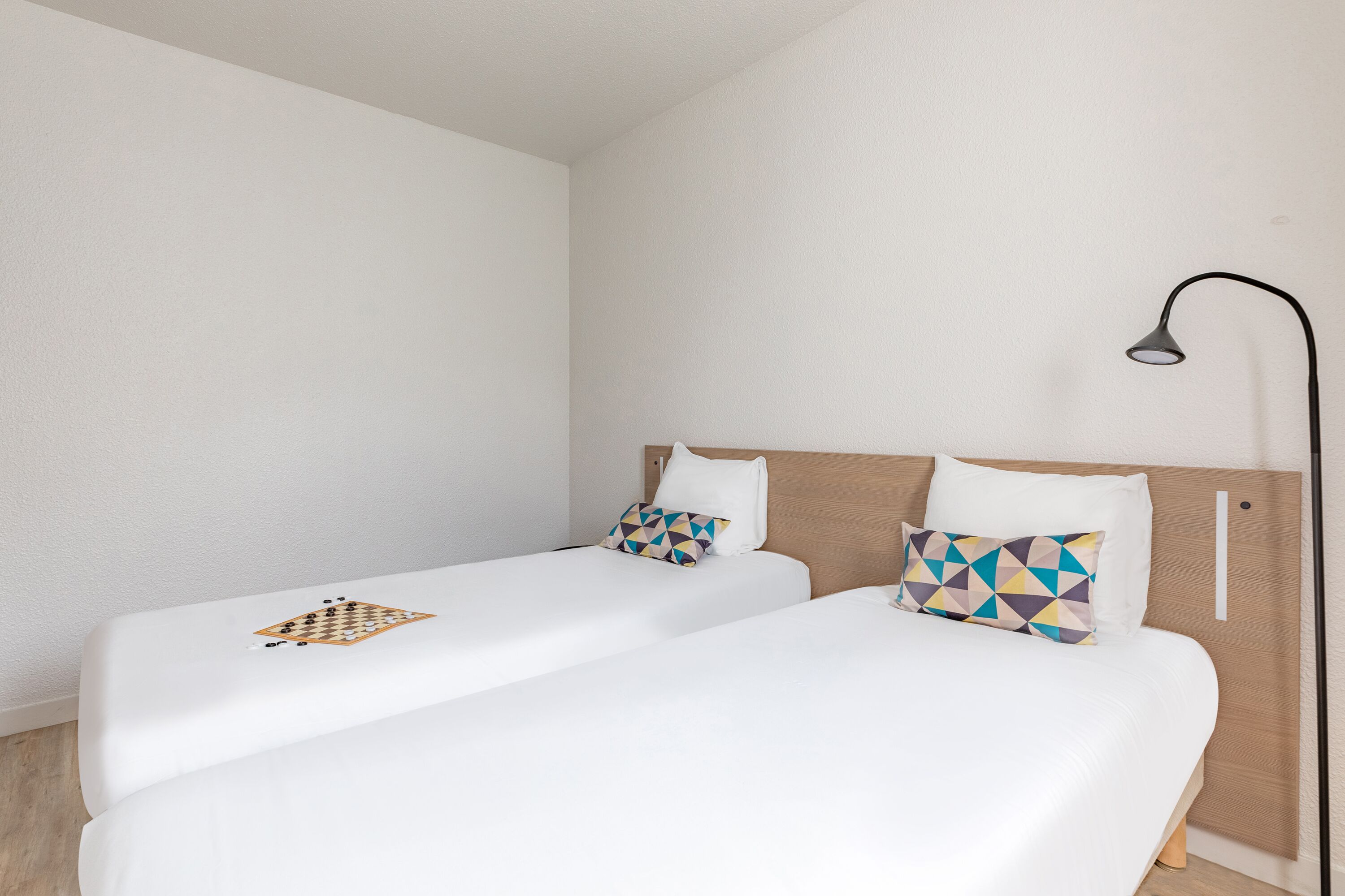 A hotel room with two single beds, each with a pillow and a chessboard.