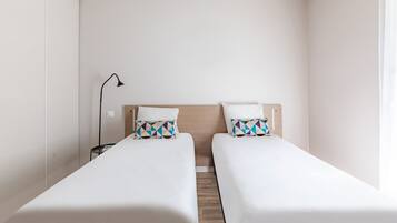 A hotel room with two single beds, a bedside table, a lamp, and a wooden floor.
