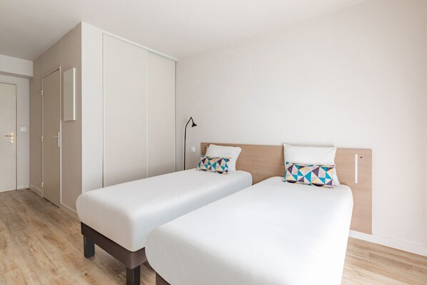 A hotel room with two single beds, a wardrobe, and a bedside lamp.